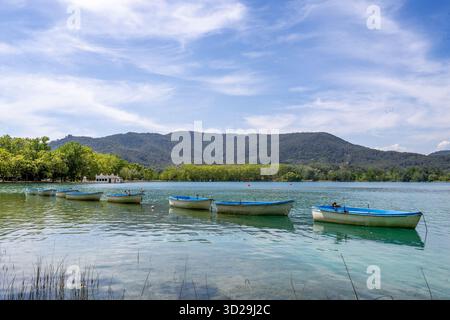 Bateaux à rames flottant sur les eaux turquoises calmes du lac de Banyoles, Catalogne, Espagne, avec des montagnes sous un ciel bleu Banque D'Images