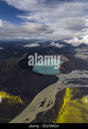 Vue aérienne du lac turquoise niché dans la caldeira volcanique noire et dure, embrassée par la mousse verte vibrante et la rivière qui coule, Highlands of Ice Banque D'Images