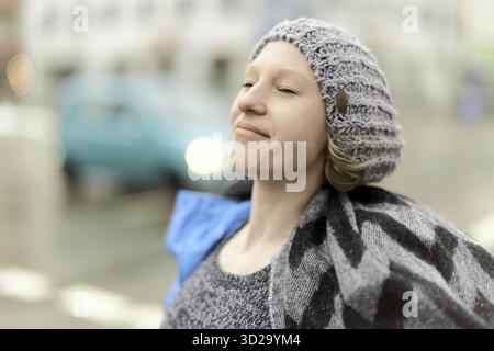Femme profitant de la brise froide d'hiver à la ville à côté de la circulation avec des sceptiques souriants sur la pollution de l'air, les températures froides gelant les voies respiratoires de son nez, Banque D'Images