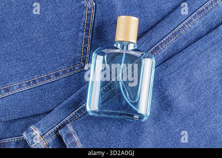 Bouteille transparente avec liquide pour hommes de parfum bleu, lotion faciale, eau de toilette sur fond bleu de tissu denim. vue de dessus. Une maquette de bouteille vierge Banque D'Images