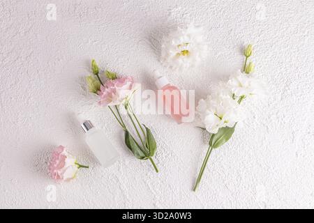 Deux bouteilles cosmétiques mates avec un compte-gouttes avec un produit de soins de la peau naturel pour le visage sur un fond blanc parmi les fleurs printanières délicates. Pose à plat Banque D'Images