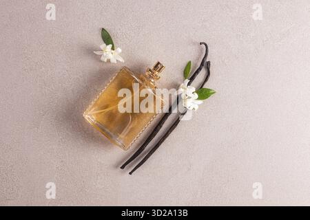 Bouteille élégante de spray cosmétique ou de parfum au parfum délicat de vanille sur un fond beige avec des bâtons de vanille naturelle et des fleurs Banque D'Images