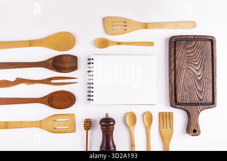 Une page blanche d'un cahier, un livre de recettes parmi les ustensiles de cuisine en bois, une planche à découper. Vue de dessus. Espace pour le texte de cuisson. Pose à plat Banque D'Images
