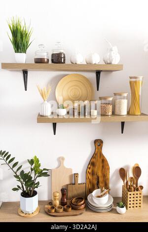 Vue verticale avant des étagères en bois de cuisine ouverte et des parties du comptoir avec divers ustensiles de cuisine, des pots de stockage, des plantes en pots Banque D'Images