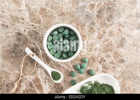 Poudre de spiruline verte biologique et comprimés d'algues vertes dans un bol blanc et une cuillère sur une table en marbre. Vue du dessus. Source alimentaire de protéines vitaminées Banque D'Images