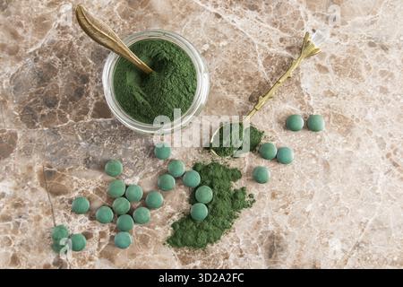 Poudre de spiruline verte dans un bocal en verre sur un fond marbré de marbre avec des comprimés de spiruline dispersés. vue de dessus. un supplément biologique sain Banque D'Images