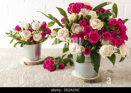 Deux seaux décoratifs en métal avec des bouquets de belles roses blanches et rouges se dressent sur des tranches rondes en bois. arrière-plan clair. vue de face Banque D'Images