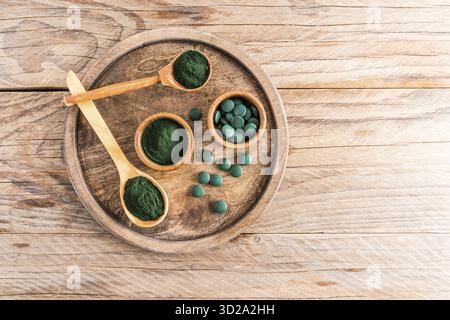 Plusieurs cuillères et bols en bois avec des comprimés de poudre et de spiruline verte sur un plateau en bois. Table rustique. Excellent additif alimentaire Banque D'Images