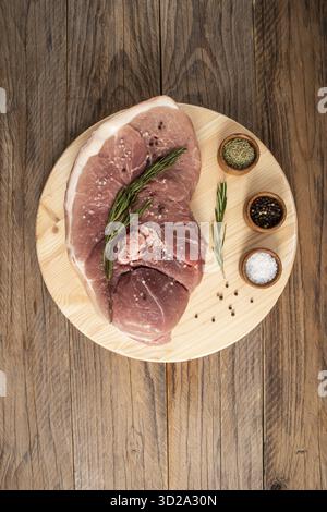 La chair du porc sur l'os repose sur une planche à découper et une table en bois avec un brin de romarin . Vue de dessus verticale Banque D'Images