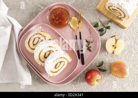 Trois morceaux de gâteau éponge roulé aux pommes maison sont servis sur une assiette en céramique rose et un plateau. Snack dessert, snack. vue de dessus. fond gris Banque D'Images
