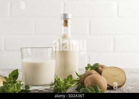 Le lait de légumes vegan des pommes de terre est une nouvelle tendance dans la nourriture. Bouteille de lait en verre face d'un mur de brique blanche Banque D'Images