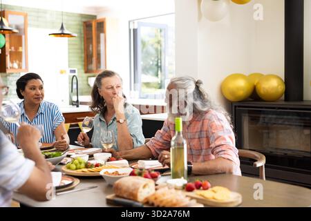 Autour de la table à manger, amis seniors ayant du vin et parlant à la maison. fête, amitié, célébration, conversation, socialisation, loisirs || autorisation du modèle Banque D'Images
