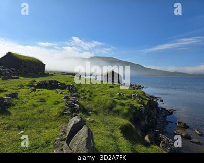 Paysage tranquille avec des cabanes en pierre traditionnelles le long de la côte des îles Féroé. Banque D'Images