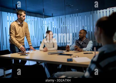 Groupe de divers collègues ayant une discussion sérieuse autour d'une table de conférence, dirigé par un manager barbu, représentant le travail d'équipe, le leadership et le développement de la stratégie dans un environnement d'affaires moderne || modèle libéré Banque D'Images