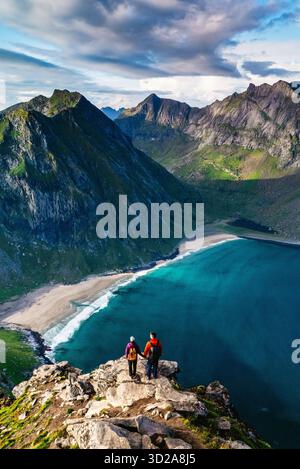 Les randonneurs profitent de vues époustouflantes depuis le sommet de Ryten sur le sentier de la plage de Kvalvika à Lofoten, en Norvège. Les eaux turquoises sereines et les montagnes escarpées créent une toile de fond parfaite pour l'aventure. || autorisation du modèle Banque D'Images
