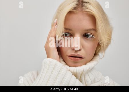 Une jeune femme blonde aux cils blancs pose dans un studio confortable dans un pull tricoté. Banque D'Images