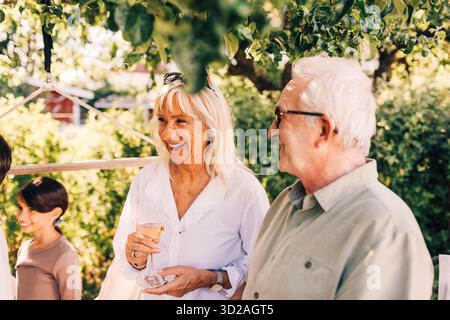Femme âgée heureuse tenant du verre de vin debout à côté de l'homme dans la fête de jardin Banque D'Images