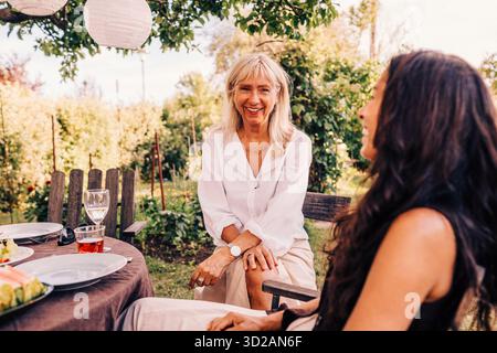 Heureuse femme senior parlant avec une amie féminine tout en étant assis à la table à manger dans la cour arrière Banque D'Images