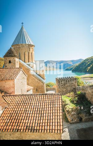 Anciens bâtiments en pierre avec des tours et des toits de tuiles surplombant un lac de montagne turquoise et des collines boisées sous un ciel bleu clair par une journée ensoleillée Banque D'Images