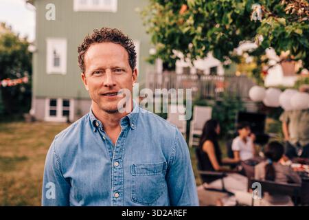 Portrait d'un homme souriant portant une chemise en denim dans la cour arrière Banque D'Images