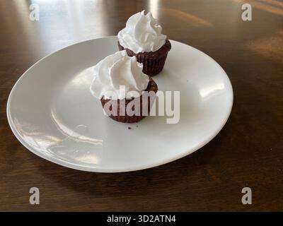 Deux petits cupcakes au chocolat à la crème fouettée sur une assiette blanche sur une table brune Banque D'Images