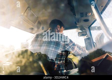 Vue arrière d'un agriculteur conduisant un tracteur dans un champ vu à travers la vitre Banque D'Images