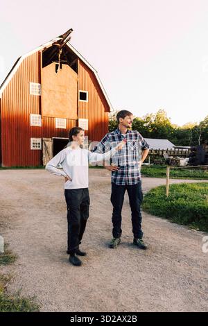 Femme expliquant fermier mâle debout avec des bras akimbo sur le sentier en face de la ferme Banque D'Images