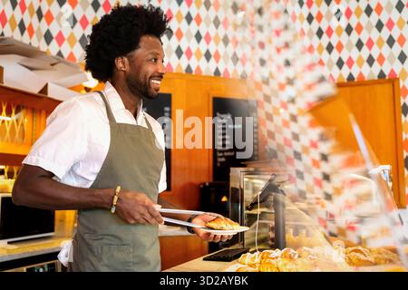 Barista masculin souriant servant des croissants frais au café Banque D'Images