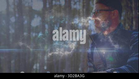 Homme assis regardant devant dans la forêt de pins, avec gilet matelassé, chemise à carreaux, lunettes, espace de copie Banque D'Images