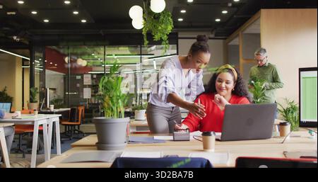 Collaboration de deux collègues femmes partageant des idées dans un bureau ouvert, avec un ordinateur portable et des tasses à café Banque D'Images