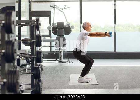 Plan de profil complet d'un homme âgé qui s'entraîne avec des haltères dans un gymnase Banque D'Images