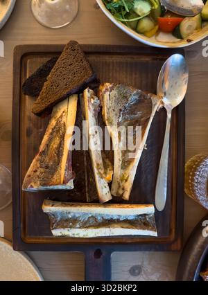 Apéritif traditionnel à la moelle osseuse servi sur une planche de bois avec pain de seigle foncé et salade de légumes Banque D'Images
