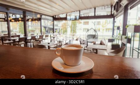 Tasse de café sur le comptoir en bois à l'intérieur d'un café moderne avec intérieur lumineux, lumière naturelle et atmosphère chaleureuse, parfait pour le style de vie ou l'hospitalité conce Banque D'Images