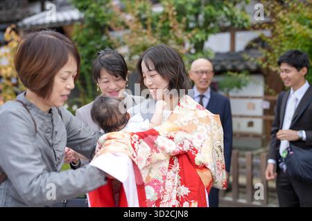 Un groupe de personnes se tient dehors, l'une d'entre elles tenant un bébé. Le bébé porte une tenue rouge et blanche Banque D'Images