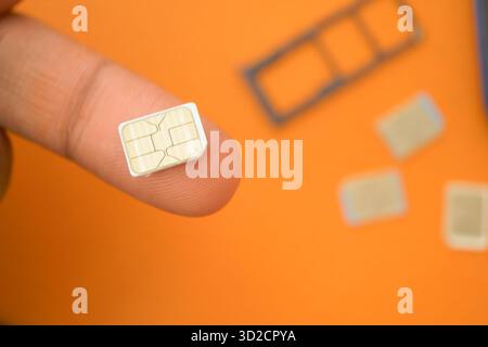 Carte SIM maintenue par un doigt sur un fond orange Banque D'Images