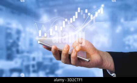 Un professionnel des affaires tient un smartphone affichant des graphiques et des graphiques financiers, symbolisant le rôle de la technologie moderne dans l'analyse des données et l'investissement Banque D'Images