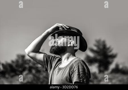Cow-boy américain. Chapeau de cow-boy en cuir. Portrait d'un jeune homme portant un chapeau de cow-boy. Des cowboys en chapeau. Beau macho barbu. Noir et blanc Banque D'Images