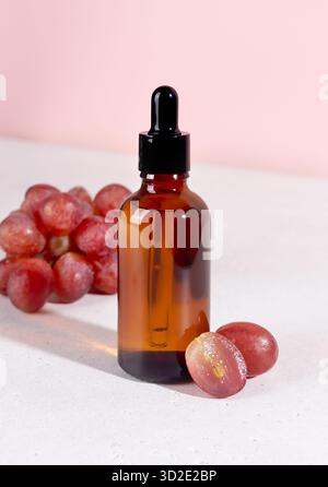 Huile de pépins de raisin dans une bouteille compte-gouttes avec des raisins rouges. Aromathérapie de soin de la peau sur fond rose Banque D'Images