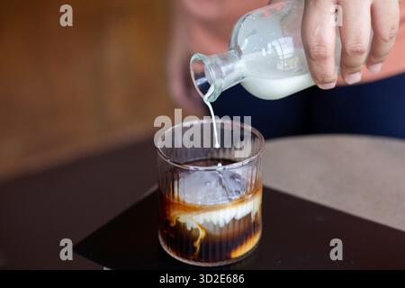 Focus sélectif verre clair café noir en verre clair Ajout de lait frais au verre ressentez l'arôme et la douceur du café mélangés à mi blanc frais Banque D'Images