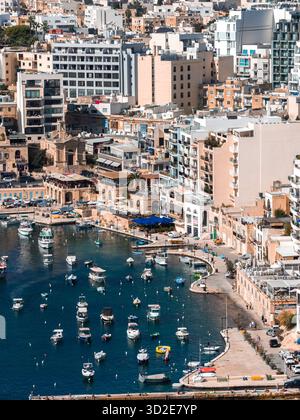 Vue aérienne de la baie de Spinola à St Julians, Malte montre un port courbe avec des bateaux de pêche, des hôtels et des appartements, des façades en calcaire, une petite chapelle, une Banque D'Images