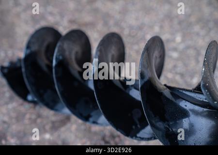 Détail de lame de foret à vis sans fin à usage intensif avec surface réfléchissante humide montrant la spirale en acier utilisée pour le forage du sol, le pieu et les opérations sur les chantiers de construction Banque D'Images