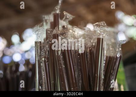 Vue rapprochée de nombreuses pailles à boire en plastique brun enveloppées dans un emballage transparent. les pailles jetables se tiennent dans un récipient prêt à être utilisé dans un café ou une restauration Banque D'Images