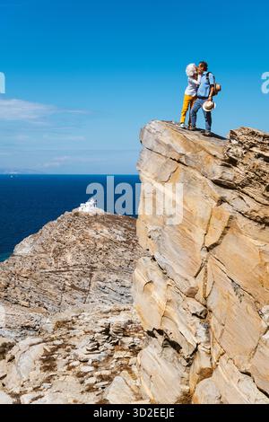 Un couple se tient sur un pic rocheux en face du phare dans la réserve naturelle du parc de Paros et baisers, en Grèce Banque D'Images
