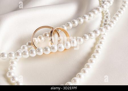 Paire de bagues de mariage en or couché sur une chaîne chic de perles de perle sur satin beige. Modèles de cartes postales, invitations. fond de mariage Banque D'Images