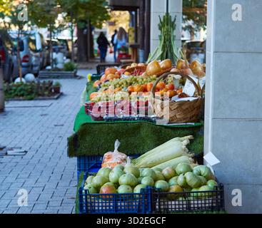 Scène de marché animée avec une gamme de fruits et légumes frais exposés dans des paniers tissés et des caisses, avec des acheteurs qui naviguent à proximité et créent Banque D'Images