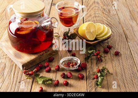 Une grande théière en verre avec bouillon de rose musquée et citron sur une table de village en bois avec des hanches de rose sèches. boisson saine Banque D'Images
