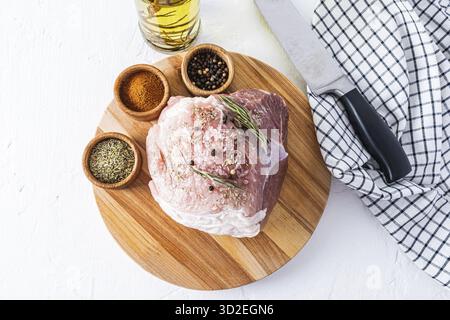 Un grand morceau de porc frais pour la cuisson repose sur une planche de bois ronde avec diverses épices. vue de dessus. fond blanc Banque D'Images