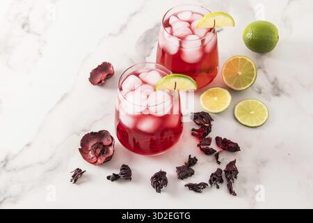 Deux verres en verre avec thé à la rose hibiscus et avec beaucoup de glace, tranches de citron vert. boisson glacée assoiffée par temps chaud. fond de marbre Banque D'Images