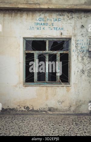 Une fenêtre cassée d'un ancien café dans un bâtiment abandonné dans la vieille ville de Marpissa, Paros, Grèce Banque D'Images