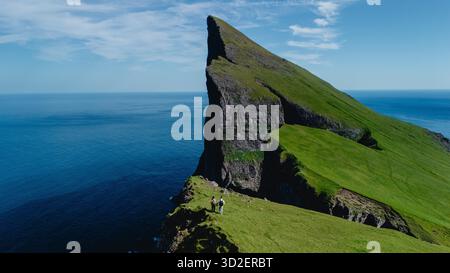 Deux aventuriers se tiennent au bord de la falaise de Mylingur dans les îles Féroé, entourés par une vue imprenable sur l'océan et des paysages verdoyants. C'est une journée parfaite pour l'exploration et la découverte. Banque D'Images